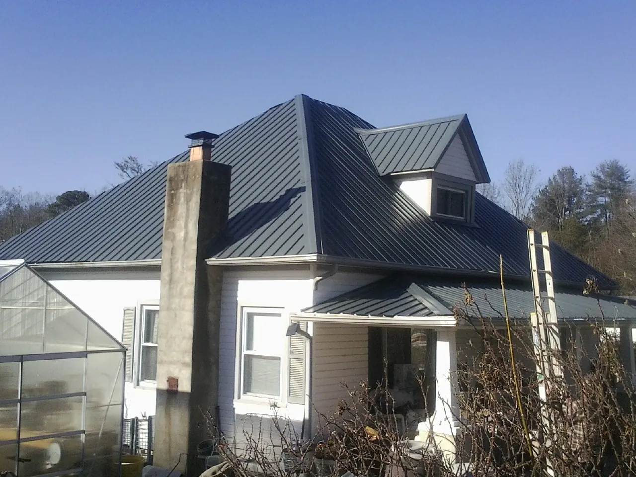 Dark blue standing seam metal roof on a white farmhouse with dormer — Slate & Tile Roof Repair by Roofing Brothers in Brunsville