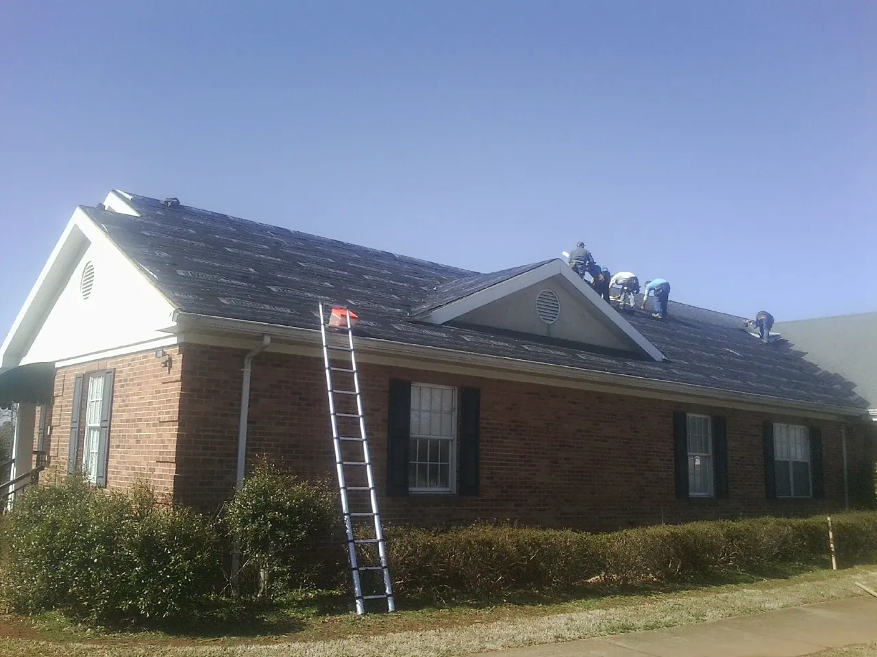 Crew tearing shingles off a brick ranch roof with a ladder set — Emergency Roof Repair work by our crew in Brunsville
