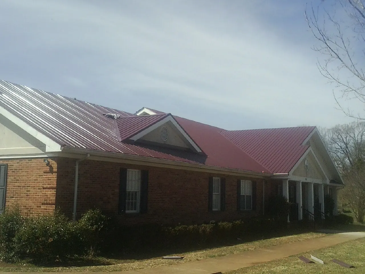 Red metal roof with gabled entries on a long brick building, from a Hail Damage Roof Repair job in Brunsville