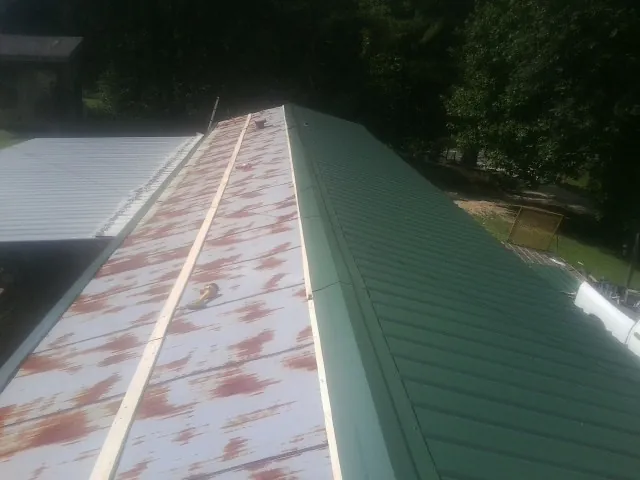Old rusted panels beside newly installed green metal roofing — Wind Damage Roof Repair by Roofing Brothers in Brunsville