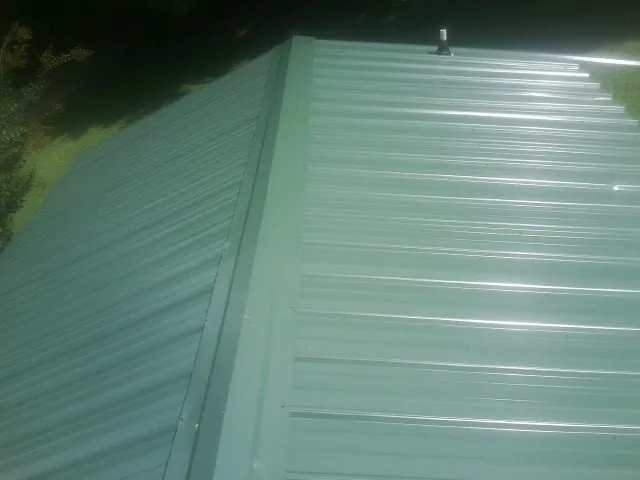 New green metal panels meeting at the ridge of a roof — Flat Roof Repair work by our crew in Brunsville
