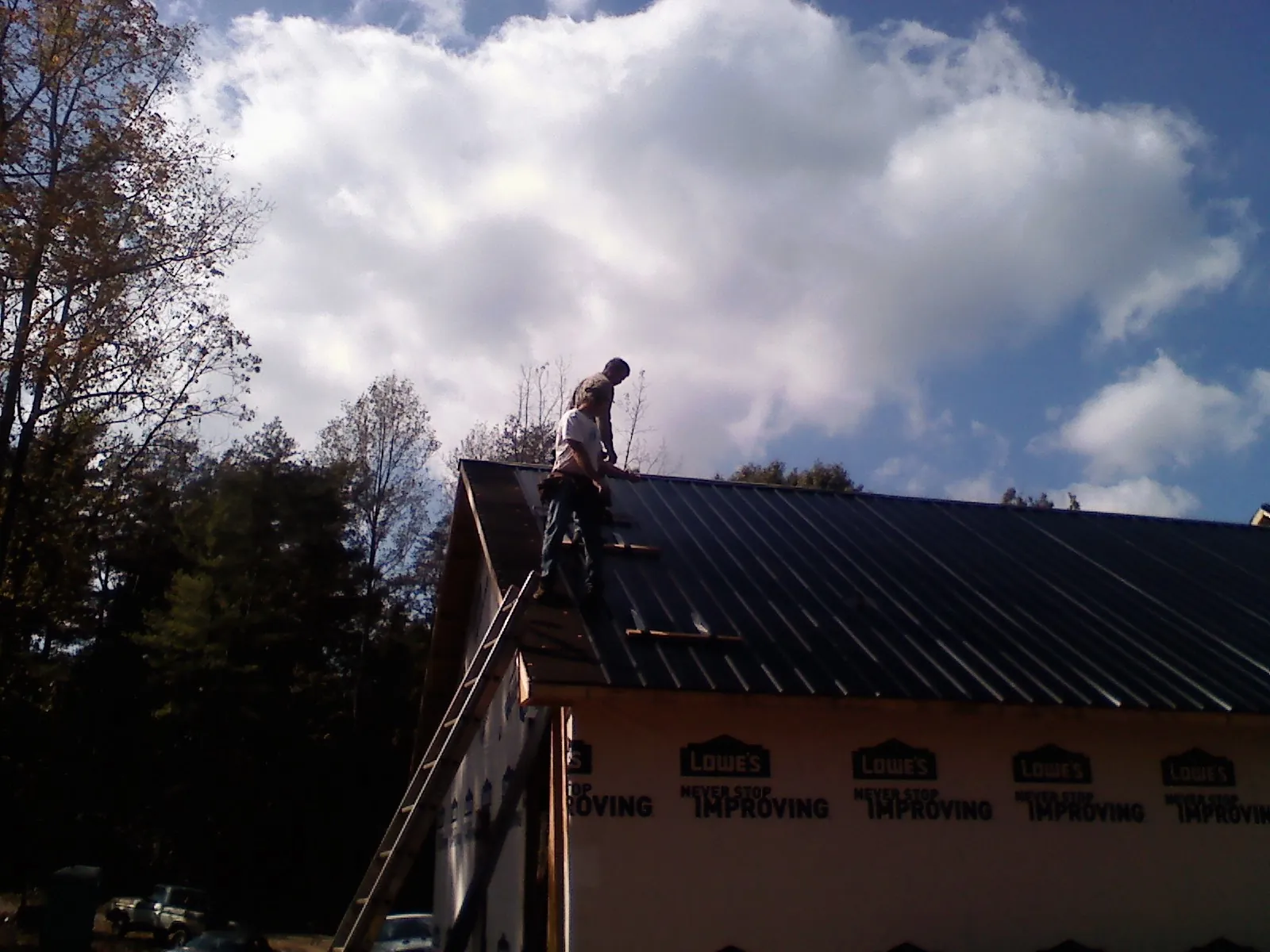 Roofer fastening dark metal panels high against a cloudy sky, from a Roof Inspection job in Brunsville