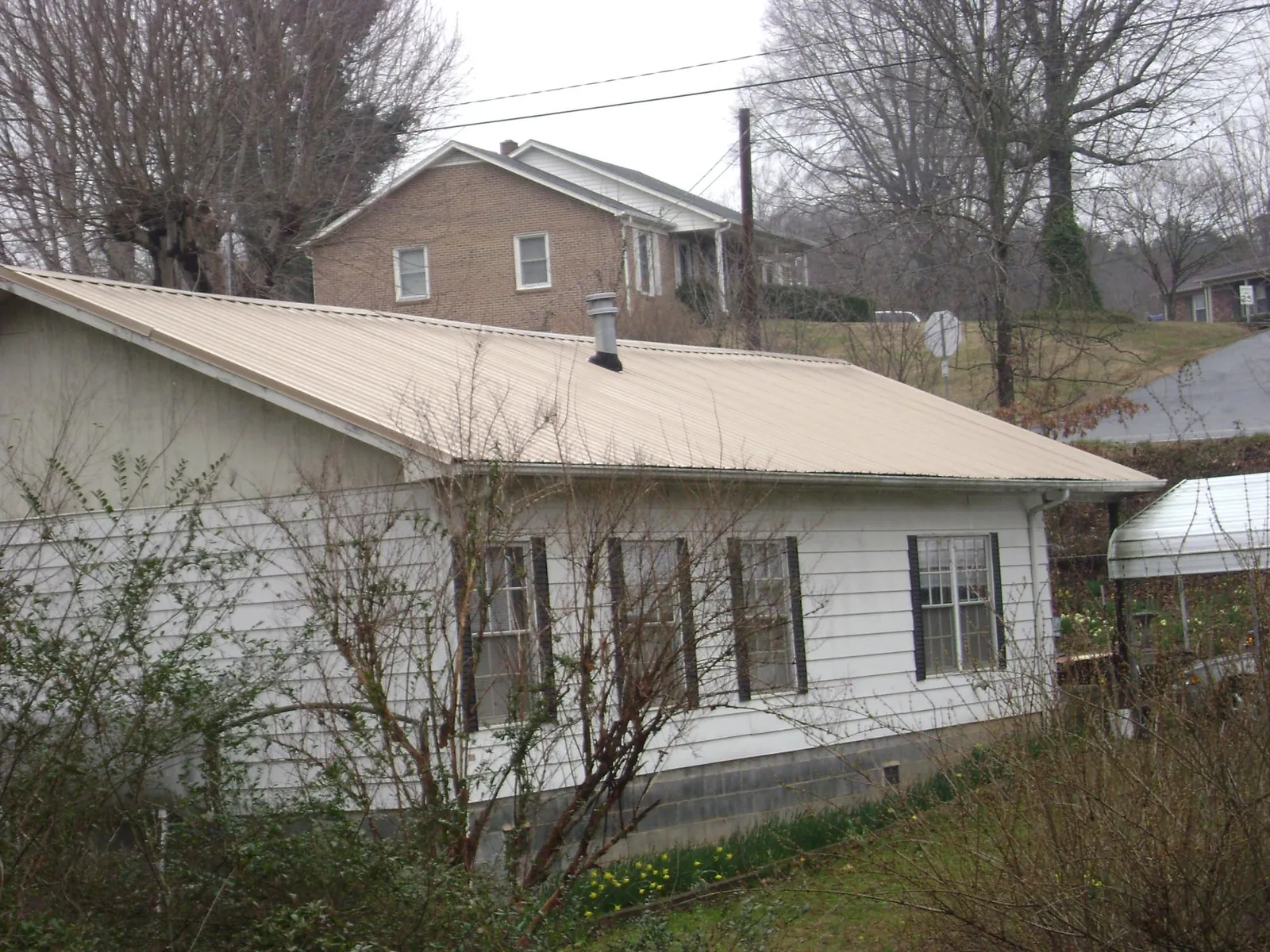 Tan metal roof on a white sided house set into a hillside — Commercial Roofing by Roofing Brothers in Brunsville