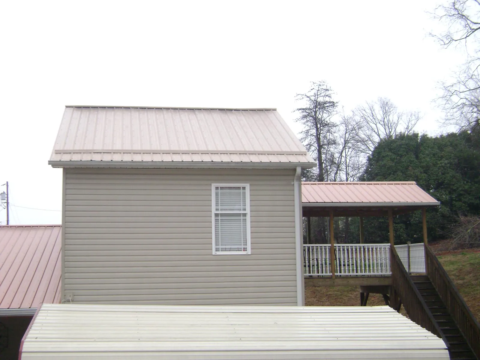 Tan metal roofs on a two story addition and attached porch, from a Roof Replacement job in Brunsville
